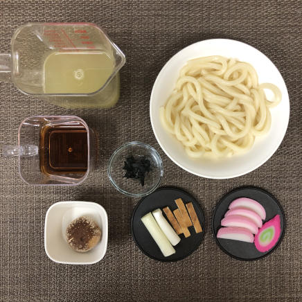 丼1杯分のおかめうどんの材料（うどん・かまぼこ・なると・ネギ・板麩・しいたけ・乾燥わかめ・めんつゆ・かつお昆布だし）