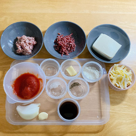 1人前の豆腐のラザニアの材料(シュレッドチーズ、絹豆腐、牛ひき肉、豚ひき肉、玉ねぎ、トマト缶、にんにく、ウスターソース、オリーブオイル、塩、コショウ、小麦粉、バター)