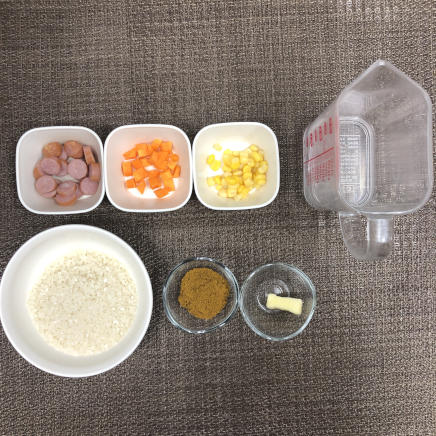 1人前のカレーピラフに使用した材料（米・ウインナー・にんじん・コーン・バター・水・カレー粉）