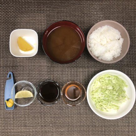 1人前のヒレカツ定食につかった材料(ご飯・わかめの味噌汁・キャベツの千切り・和風ドレッシング・ウスターソース・沢庵・レモン・からし)