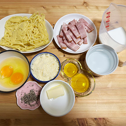 大皿1皿分の生パスタのカルボナーラの材料（生パスタ、ベーコン、卵、パルメザン、オリーブオイル、バター、牛乳、黒こしょう、水）