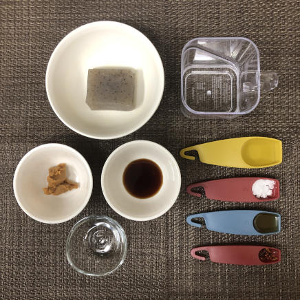 小皿1皿・1人前のこんにゃくの甘辛煮の材料（こんにゃく・水・鷹の爪(輪切り)・酒・みりん・醤油・味噌・砂糖・ごま油）