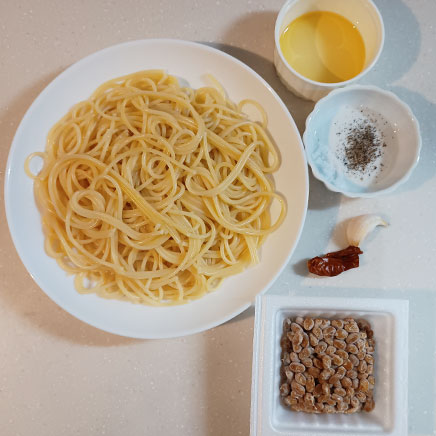 中皿1皿分の納豆ペペロンチーノに使用した材料(パスタ、納豆、オリーブオイル、にんにく、塩、黒こしょう、唐辛子)