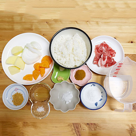 大皿１皿分の米粉カレーに使った材料（豚肩ロース、玉ねぎ、人参、じゃがいも、サラダ油、塩、おろしにんにく、おろし生姜、カレー粉、水、米粉、コンソメ、砂糖、ご飯）